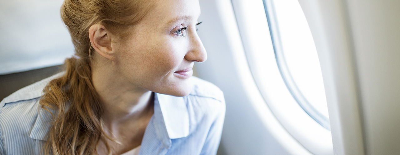 Eine Passagierin schaut entspannt aus dem Fenster eines Flugzeugs