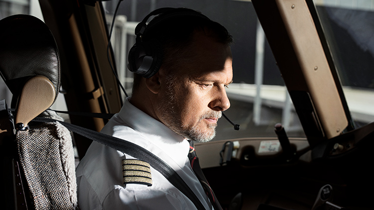 An elderly pilot with a full beard looks intently at  Instruments in an aircraft cockpit