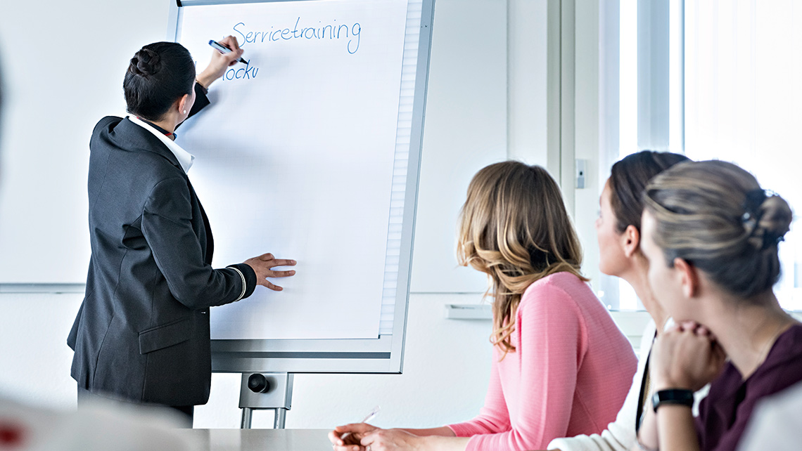 Eine Trainerin schreibt in einem Seminar mit drei Teilnehmerinnen 